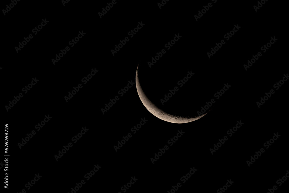 A narrow crescent of the waning moon in the night sky. A narrow crescent of the waning moon in the night sky.
