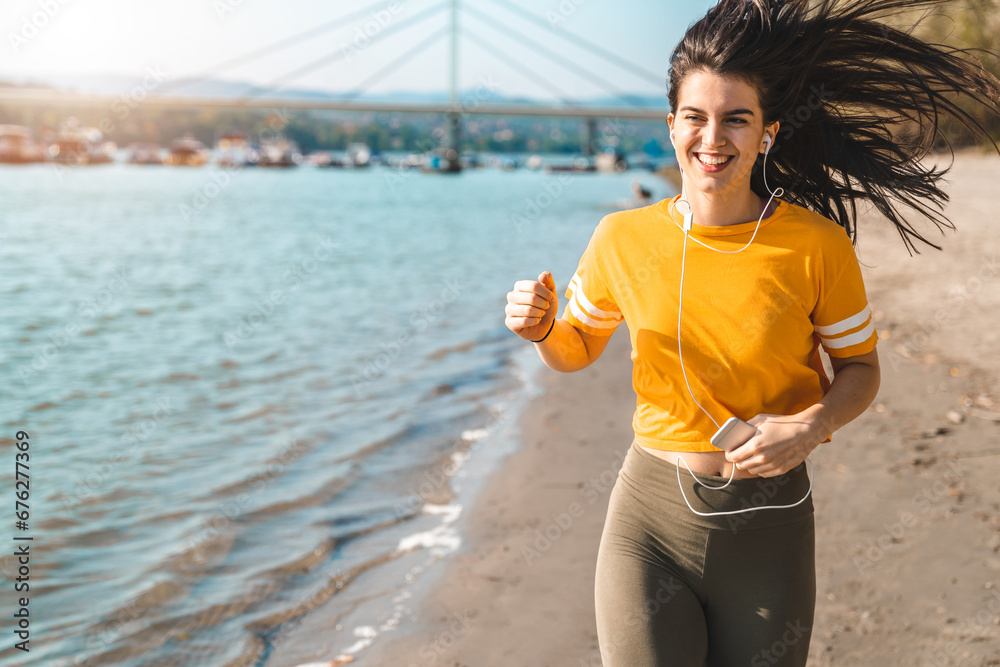 Attractive smiling female fitness instructor running by the seaside on a sunny day in autumn. Attractive smiling female fitness instructor running by the seaside on a sunny day in autumn.