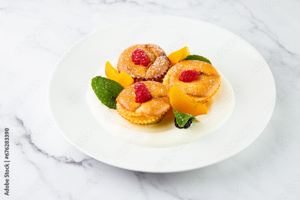 muffins with peach, raspberry, black berry and mint covered with powdered sugar, side view muffins with peach, raspberry, black berry and mint covered with powdered sugar, side view