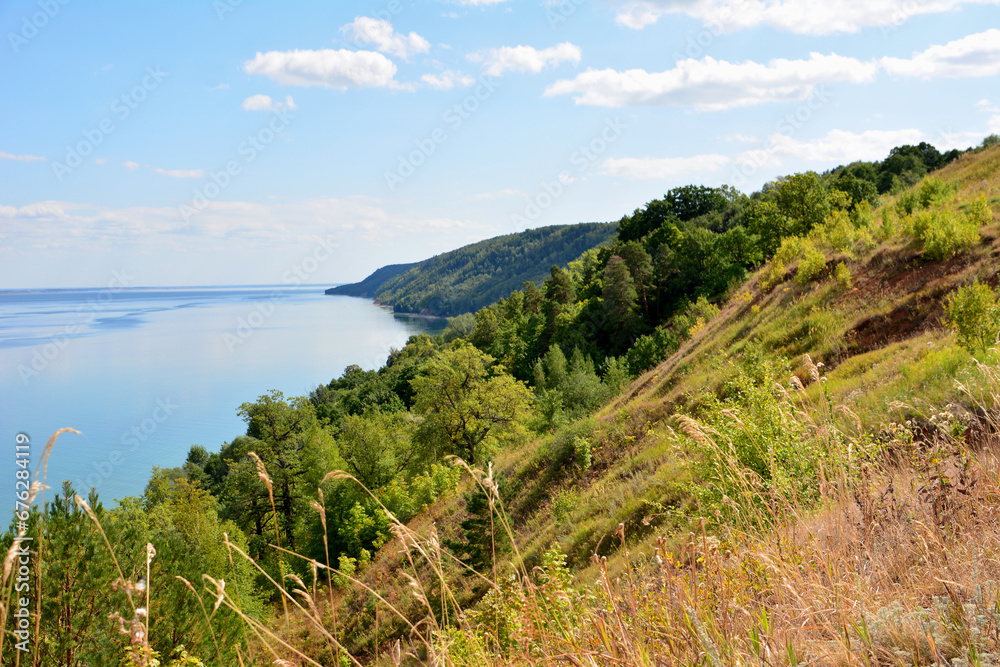 hillside with green trees and blue lake and clouds on sky copy space 