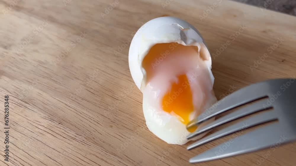 Liquid bright yellow yolk flows from boiled egg onto wooden surface of cutting board. Fork cuts egg white. Soft-boiled egg. Concept of healthy food, cooking breakfast, lunch, brunch, dinner, diet