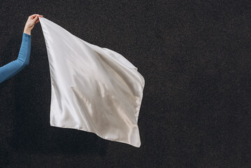 White silk scarf in woman's hand floating on the wind on dark grey background. Lifestyle.