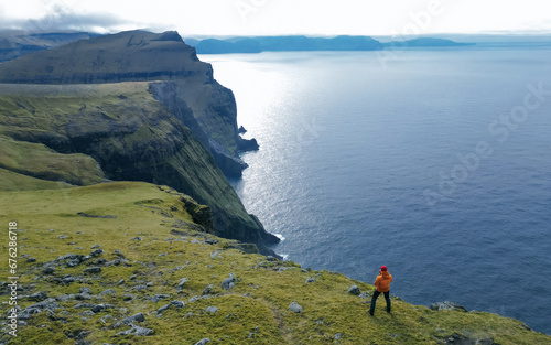 Young man hiker standing on the edge of cliff. Photo man, tourist reaching summit enjoying on view amazing ocean. Copy Space
