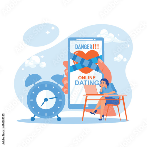 Hand holding a cell phone with a warning tape over the heart that says the dangers of online dating. A gloomy woman sits in front of a laptop with an alarm clock beside her. Online Dating concept. 