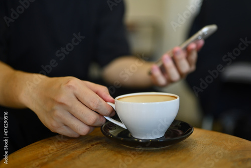 Cropped shot of man hand holding cup of coffee and using mobile phone at cafe
