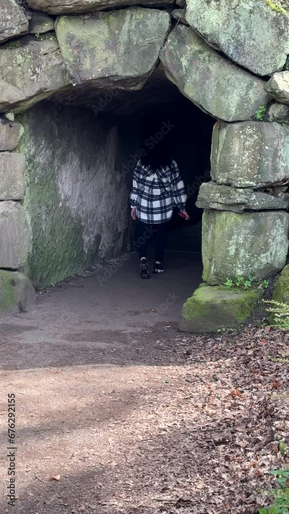 Vertical video. Rear view of long dark curly hair woman wearing checked pattern jacket and leggings entering and disappearing in arched stone tunnel. Vertical video. Rear view of long dark curly hair woman wearing checked pattern jacket and leggings entering and disappearing in arched stone tunnel.