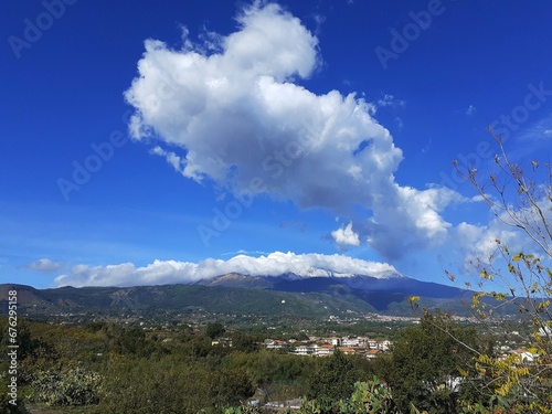 Vista panoramica dell'Etna con nuvole che la coprono e grosso nuvolone nel cielo azzurro. © Angelo Maria Trovato