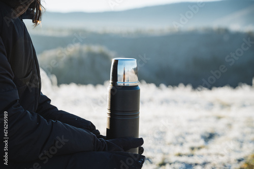 Black metal thermos on the background of winter forest, beautiful landscape, object in human hands, thermo flask for hot drinks. photo
