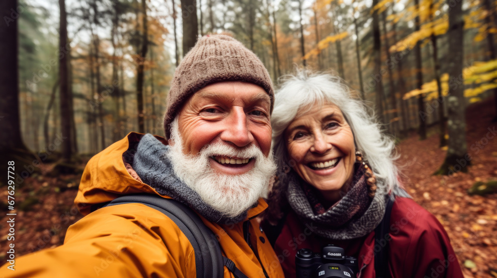 POV portrait of active senior couple looking at camera and smiling while taking selfie photo during hike in autumn forest, copy space