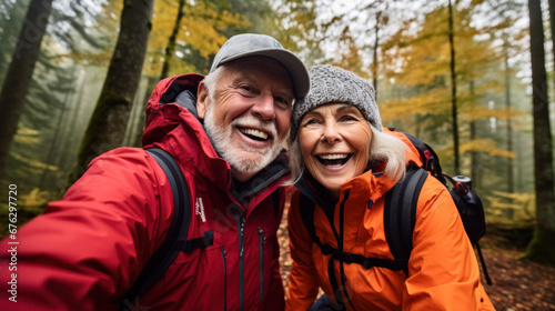 POV portrait of active senior couple looking at camera and smiling while taking selfie photo during hike in autumn forest  copy space