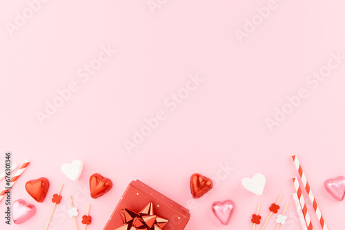 Red gift boxes with ribbons, heart shaped candies, marshmallows and paper heart decorations on pink background