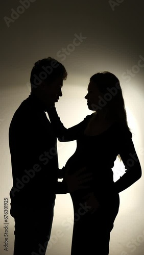a girl and a boy stand opposite each other on a black background. silhouette of a couple in love. pregnant girl replenishment in the family