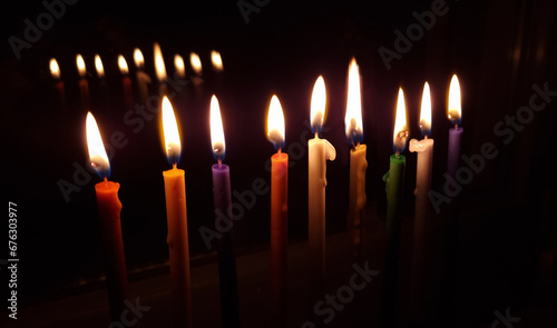 Hanukkah Menorah with eight lit colored candles and one additional candle, intended for Hanukkah, a Jewish holiday, the traditional festival of lights. On the window with reflection