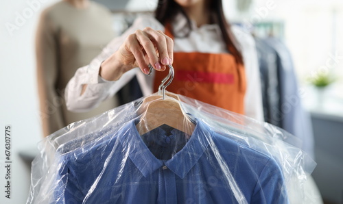 Administrator at dry cleaners keeps clean clothes on hangers in bag. Laundry and dry cleaning services concept