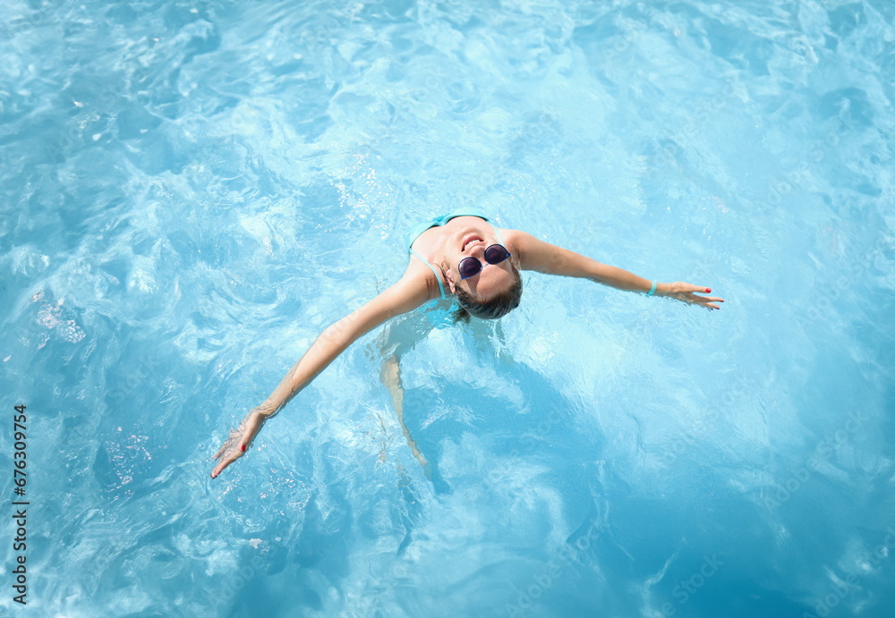Young woman in sunglasses swimming in pool top view. Rest at resort concept