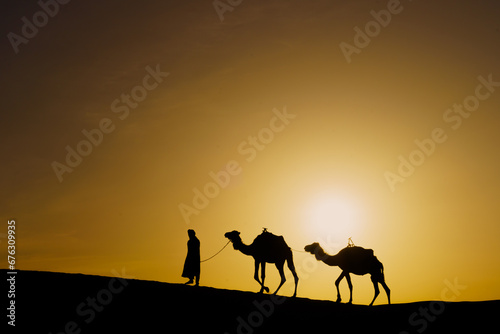 Sunrise silhouette of camels and handler  Merzouga