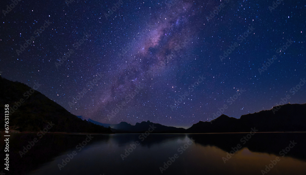 Celestial Milkyway glittering brightly above still dark water body surrounded with silhouette mountain range on clear night