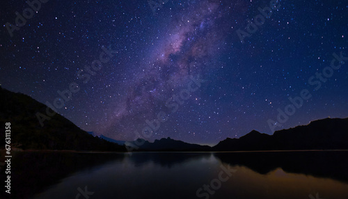 Celestial Milkyway glittering brightly above still dark water body surrounded with silhouette mountain range on clear night