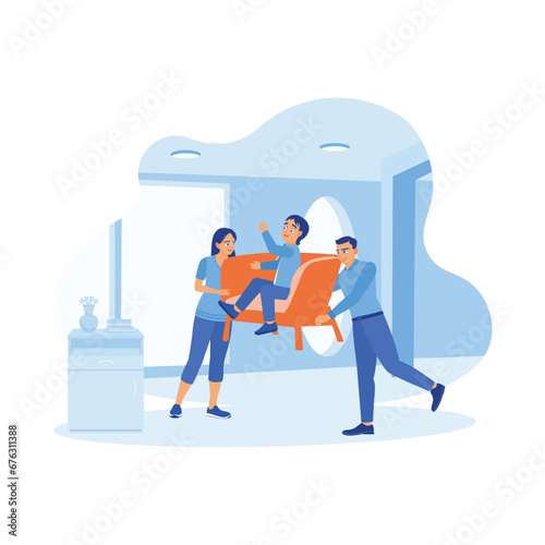 A young and cheerful husband and wife moved the armchair occupied by their son into the house. A small family moves to a new home. A couple of happy, funny parents concepts. 
