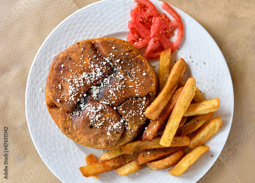 Traditional Kefalonian meat pie with French fries and two tomato slices served on the white plate. Top view. photo