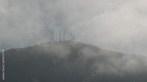 Metal turrets for receiving and transmitting satellite dishes for telecommunications and other signals on top of a mountain and partially covered by fog and low clouds.