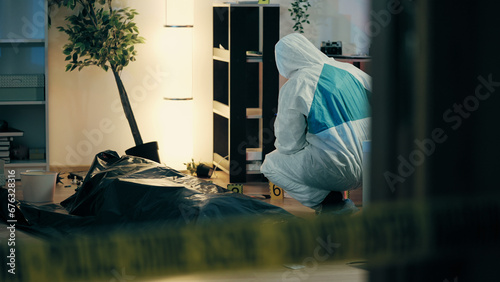 A forensic expert is collecting samples near a corpse in a body bag at the murder scene