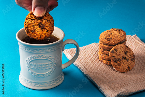 A man dunking a chocolate chip cookie in a mug of black coffee with copy space