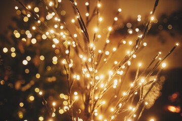 Stylish christmas illuminated tree on background of golden lights bokeh, decorated tree and burning fireplace in evening room. Atmospheric magical christmas eve at fireplace.