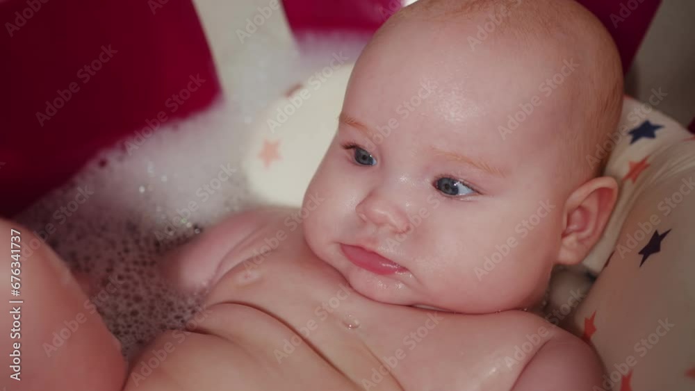 Newborn baby taking a bath in a red bathtub with foam Newborn baby taking a bath in a red bathtub with foam