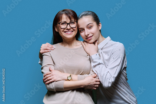 Portrait of mother and teenage daughter embracing together on blue background