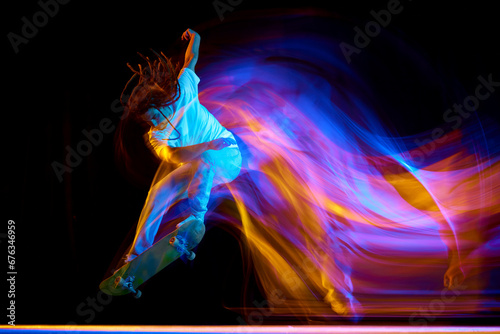 Man skateboarder performing freestyle tricks in motion isolated black background in mixed neon flashes of light. Concept of youth culture.