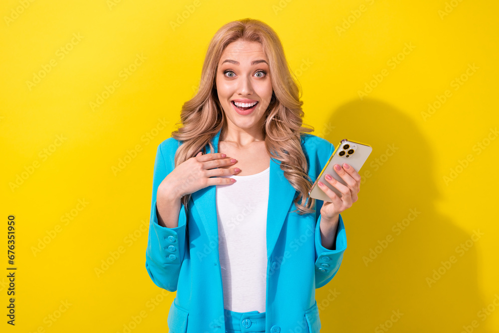 Portrait of positive impressed lady hold smart phone arm touch chest unexpected news isolated on yellow color background Portrait of positive impressed lady hold smart phone arm touch chest unexpected news isolated on yellow color background