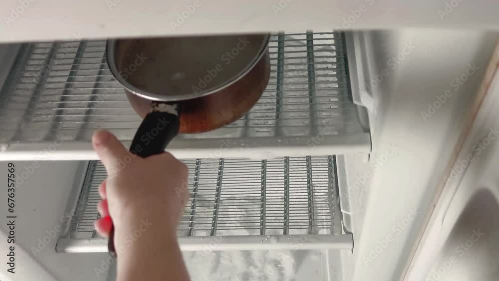Derritiendo el hielo de un congelador con la ayuda de dos cazos con agua caliente.