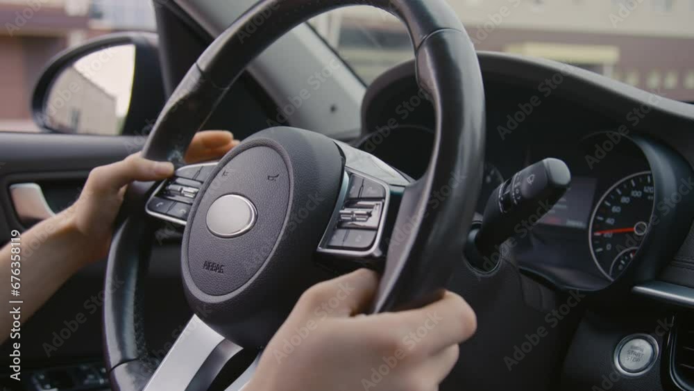 Closeup side shot of unrecognizable driver turning steering wheel while driving a car in urban area Closeup side shot of unrecognizable driver turning steering wheel while driving a car in urban area