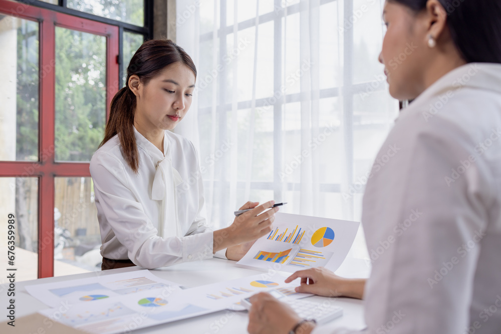 Two asian confident business women point to graphs and charts to analyze market data, balance sheet, account, net profit to plan new sales strategies to increase production capacity. Two asian confident business women point to graphs and charts to analyze market data, balance sheet, account, net profit to plan new sales strategies to increase production capacity.