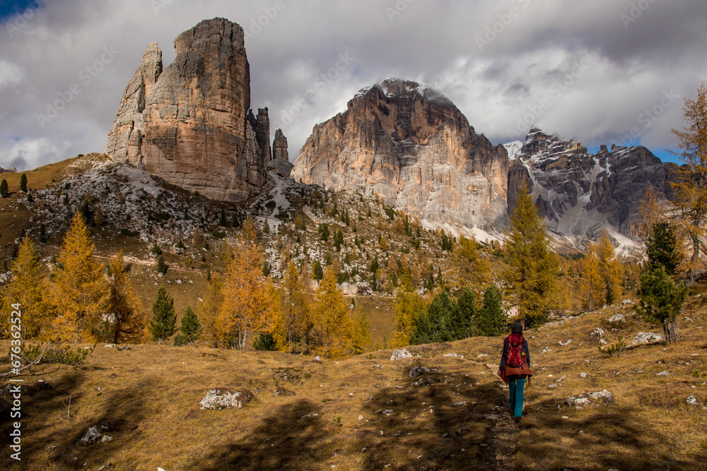 young mountaineer girl walks through a beautiful autumn landscape of golden trees and mountains towards the Cinque Torri in the Dolomite Alps