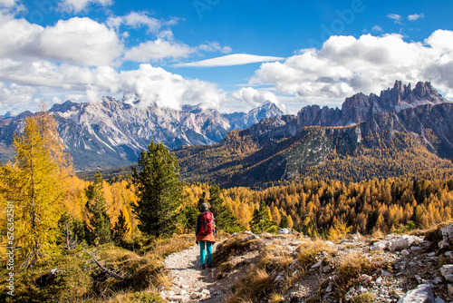 Mountaineer girl hikes through a spectacular landscape of autumn forests with golden trees and the peaks of the Croda da Lago mountain range in the Dolomite Alps photo