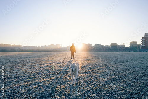 Man during morning walk with happy dog. Pet owner and his labrador retriver on field against city at frosty winter sunrise.. photo