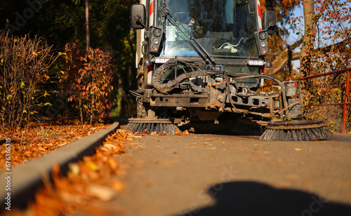 Cleaning the alleys in a park of a lot of fallen autumn leaves on the asphalt. Close up photo with a street utility car machine used to clean the public parks. © Dragoș Asaftei