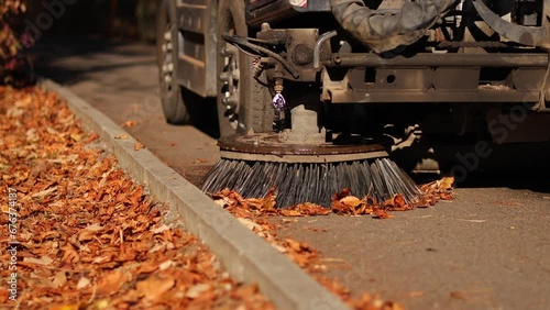 Cleaning the alleys in a park of a lot of fallen autumn leaves on the asphalt. Close up 4k video selective focus with a street utility car machine used to clean the public parks. photo