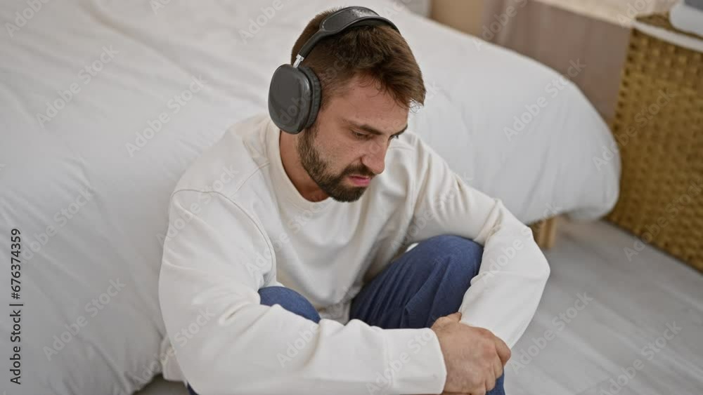 Upset young hispanic man lying comfortably on bed, deep in thought while listening to music in a relaxed morning at home Upset young hispanic man lying comfortably on bed, deep in thought while listening to music in a relaxed morning at home