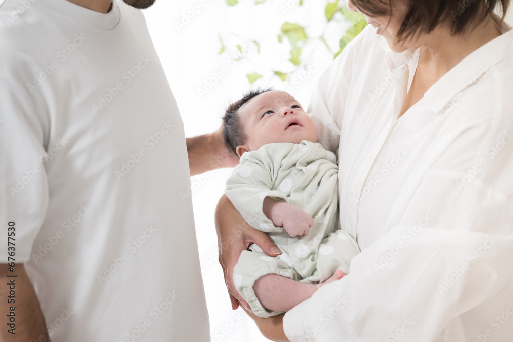 Obraz premium 明るい白い部屋で赤ちゃんを抱っこするお父さんとお母さんの幸せそうな家族顔無し 不妊治療や高齢出産などののイメージ