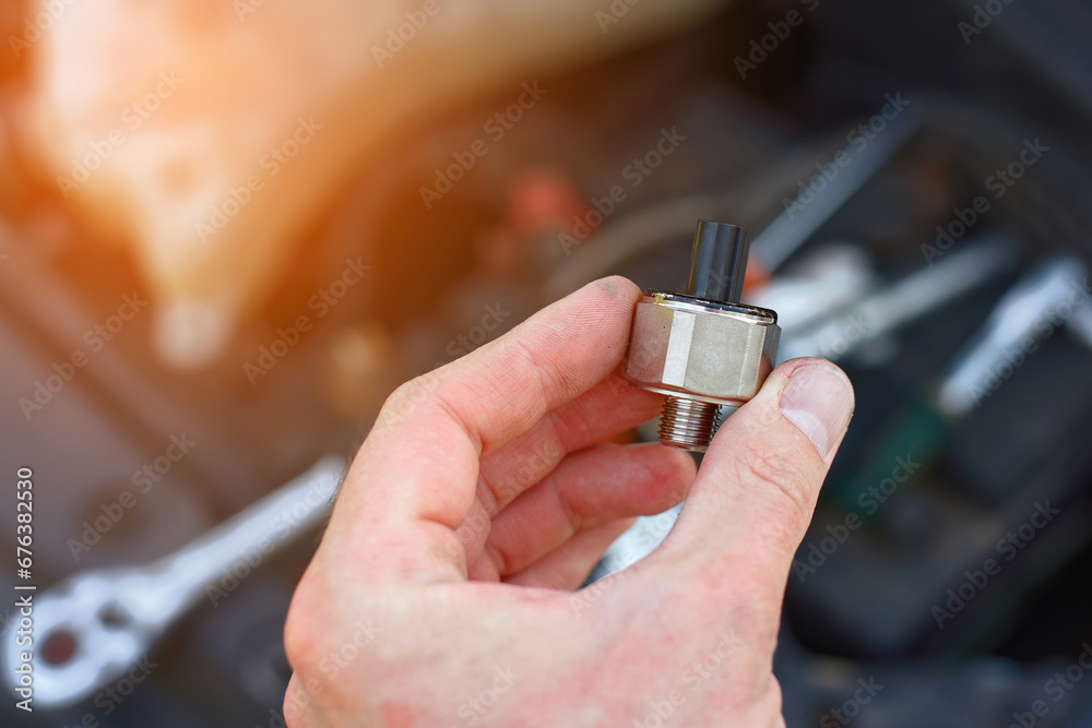 Repair man installing new knock sensor in car. Man repair broken car, engine detonation, change broken knock sensor. Electrician hold in hand new sensor, replacing faulty electric spare part.