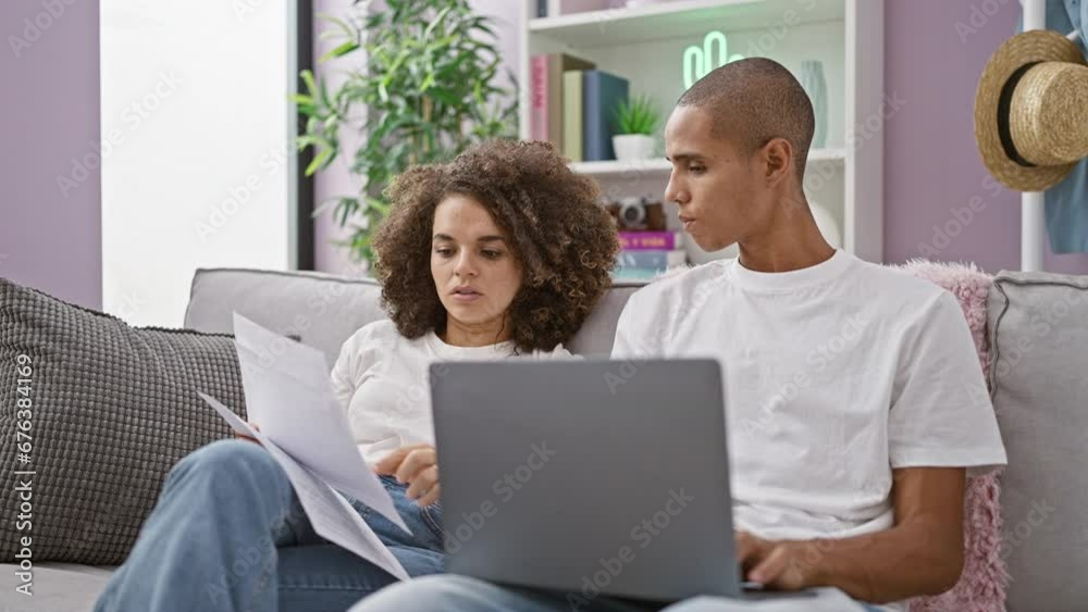 Beautiful couple casually sitting together on their home sofa, reading a serious document on their laptop, embracing their shared online lifestyle Beautiful couple casually sitting together on their home sofa, reading a serious document on their laptop, embracing their shared online lifestyle