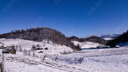Ancient romanian houses on the frozen hills in the middle of winter. Wonderful landscape in the cold season with rustic buildings at the foot of the high mountains