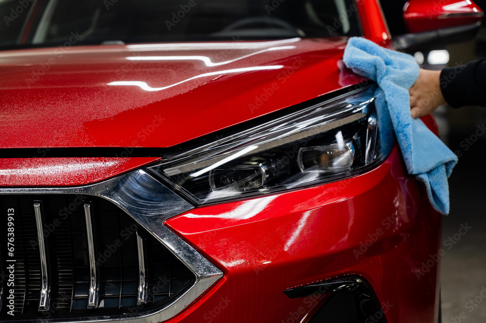 A man wipes the headlights of a red car with a microfiber cloth.