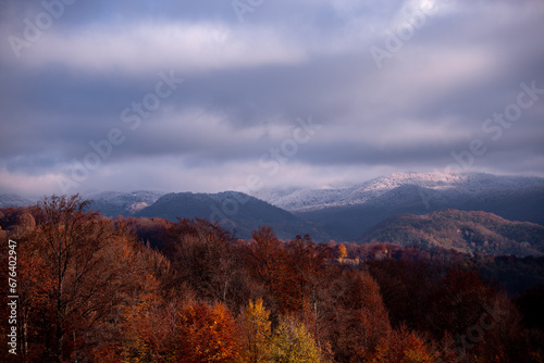 Gorgeous scenery with a wild forest full of colors in the autumn season. The border between two seasons, autumn and winter, observed on the high hills on a sunny day