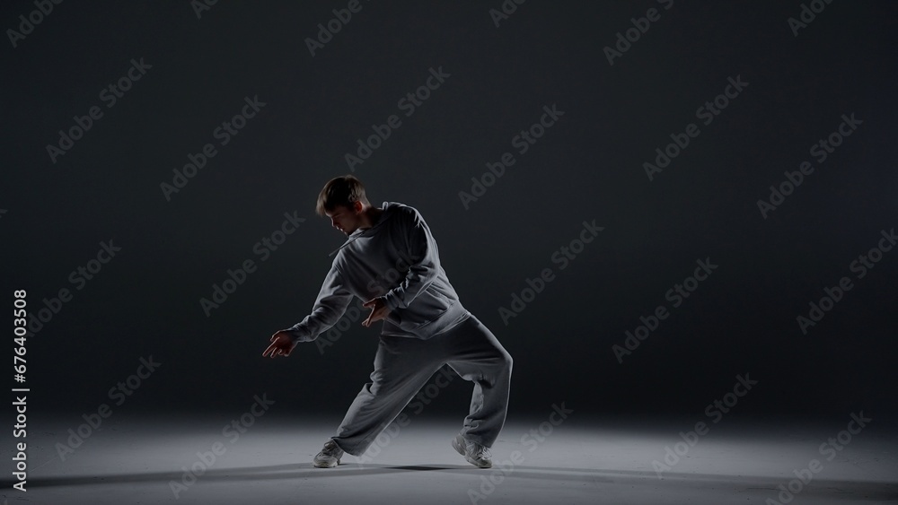 A young man stands against a dark background. He is highlighted by a white light from below. Creates a light haze. Demonstrates a dance movement by leaning to the side. He is plastic, rhythmic A young man stands against a dark background. He is highlighted by a white light from below. Creates a light haze. Demonstrates a dance movement by leaning to the side. He is plastic, rhythmic