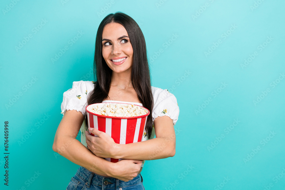 Photo of funky dreamy girl dressed white top eating pop corn looking empty space isolated teal color background Photo of funky dreamy girl dressed white top eating pop corn looking empty space isolated teal color background