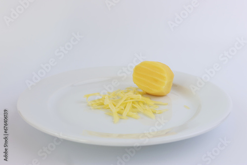 A miniature grater and grated potatoes on a white plate.